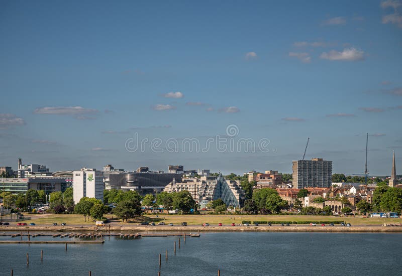 Southampton, England, UK - July 7, 2022: Harbor scenery. Mayflower green park behind dock with Holiday Inn hotel and modern residential building in back under blue sky. Southampton, England, UK - July 7, 2022: Harbor scenery. Mayflower green park behind dock with Holiday Inn hotel and modern residential building in back under blue sky