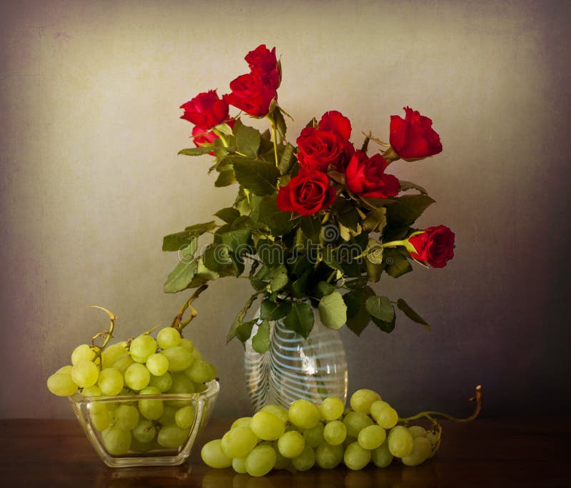 Mazzo delle rose rosse su un vaso di vetro e sull'uva sopra