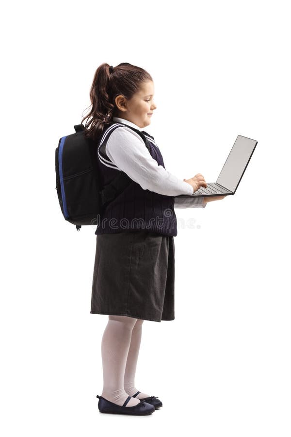 Mała uczennica w jednolitej pozycji i używać laptop. Pełny długość profilu strzał uczennica w jednolitej pozycji i używać laptop odizolowywającego na białym tle troszkę