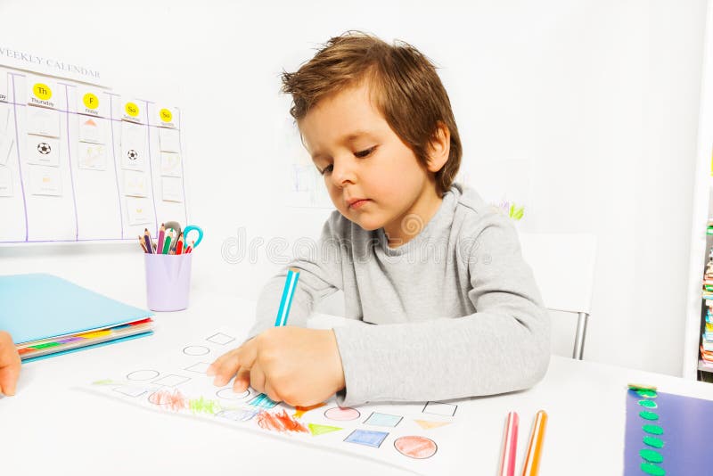 Small boy draws with pencil on the paper during Applied Behavior Analysis ABA sitting at the table indoors. Small boy draws with pencil on the paper during Applied Behavior Analysis ABA sitting at the table indoors