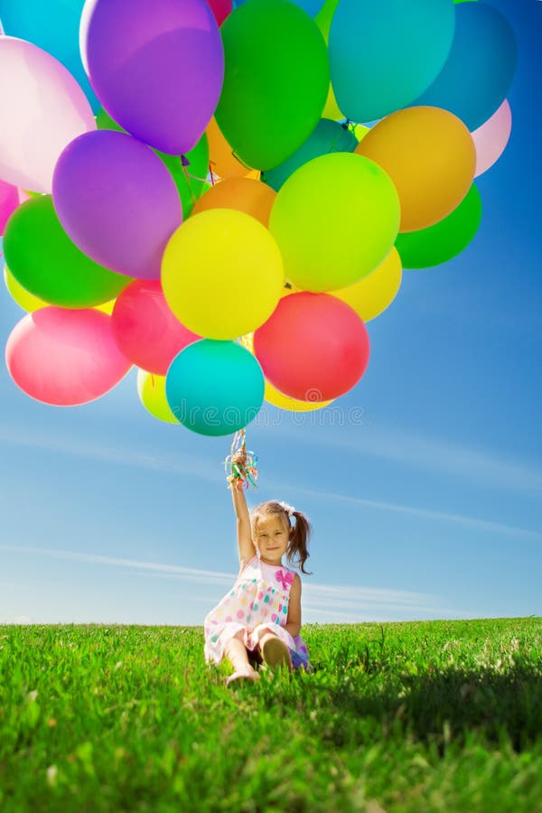 Mała dziewczynka trzyma kolorowych balony. Dziecko bawić się na zieleni zdjęcia stock Mała dziewczynka trzyma kolorowych balony. Dziecko bawić się na zieleni zdjęcia stock