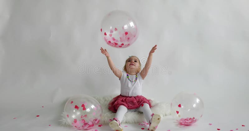 Mała 2-letnia dziewczynka bawiąca się balonem z papierami o kształcie serca w środku i wokół