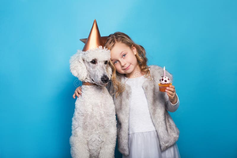 Little beautiful girl with dog celebrate birthday. Friendship. Cake with candle. Studio portrait over blue background. Little beautiful girl with dog celebrate birthday. Friendship. Cake with candle. Studio portrait over blue background