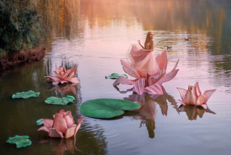 A little fabulous woman lives in a pink flower in harmony with nature. Fantasy photo session in style of girl Thumbelina. Background mystical fairytale autumn lake, green and orange trees blue water. A little fabulous woman lives in a pink flower in harmony with nature. Fantasy photo session in style of girl Thumbelina. Background mystical fairytale autumn lake, green and orange trees blue water.