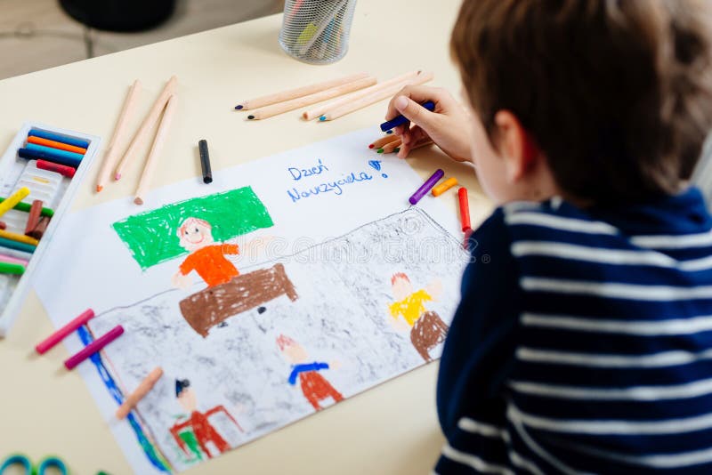 Małe dziecko rysuje pastelowego rysunek jego nauczyciel w szkolnej klasie
