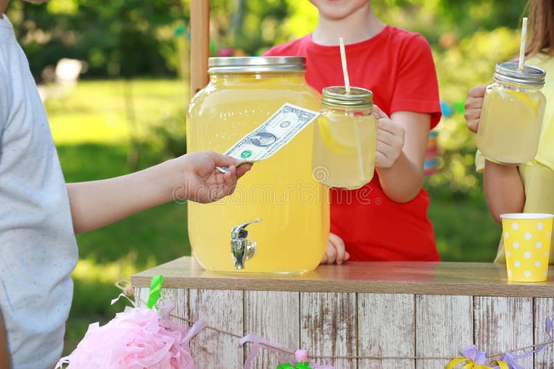 Little girls selling natural lemonade to boy in park, closeup. Summer refreshing drink. Little girls selling natural lemonade to boy in park, closeup. Summer refreshing drink