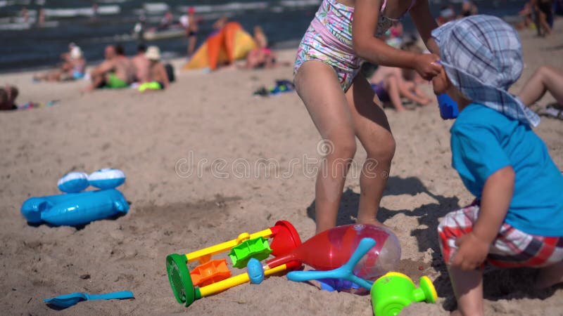 Mały chłopiec z dziewczyną bawią się zabawkami i wodą na plaży. zamazani ludzie