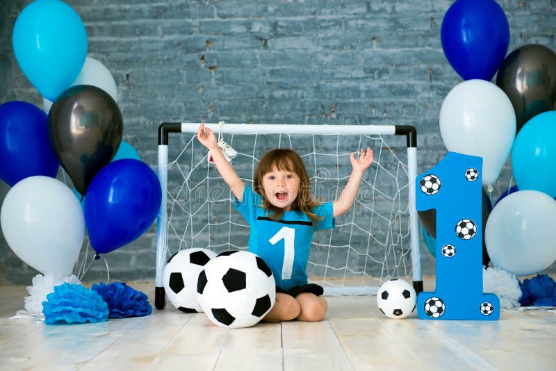 Mały rozochocony dziecko ubierał w sporta odzieżowym obsiadaniu na podłoga blisko futbolowego celu, patrzeje dużą piłki nożnej pi obraz royalty free Mały rozochocony dziecko ubierał w sporta odzieżowym obsiadaniu na podłoga blisko futbolowego celu, patrzeje dużą piłki nożnej pi obraz royalty free