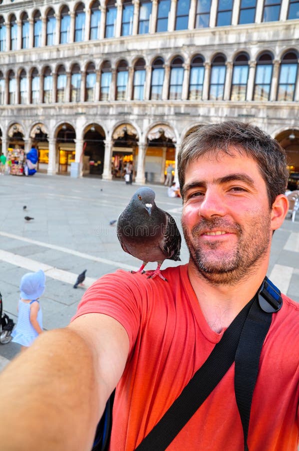 Colpo di auto di una sorridente giovane piccione sulla spalla in piedi in piazza San Marco a Venezia, Italia.