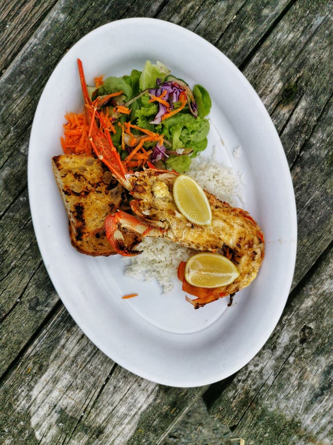 A meal of crayfish, rice and green salad on an oval plate on a rustic wooden table