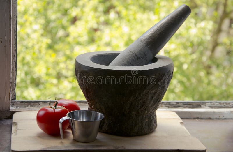 Measuring cup, tomatoes and a mortar. A steel measuring cup, two ripe, red tomatoes next to a large stone mortar with pestle on a wood cutting board by the royalty free stock images Measuring cup, tomatoes and a mortar. A steel measuring cup, two ripe, red tomatoes next to a large stone mortar with pestle on a wood cutting board by the royalty free stock images