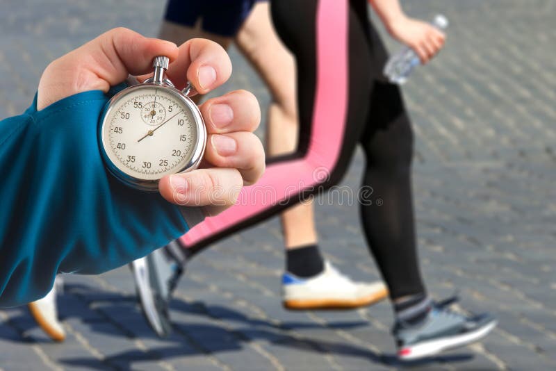 Measuring The Running Speed Of An Athlete Using A Mechanical Stopwatch.  Hand With A Stopwatch On The Background Of The Legs Of A Runner. Stock  Photo, Picture and Royalty Free Image. Image