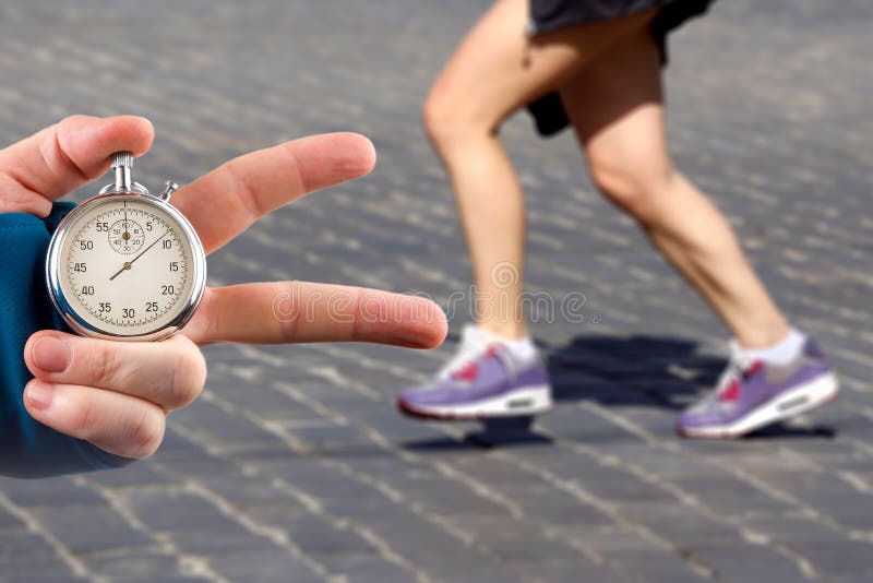 Measuring The Running Speed Of An Athlete Using A Mechanical Stopwatch.  Hand With A Stopwatch On The Background Of The Legs Of A Runner. Stock  Photo, Picture and Royalty Free Image. Image