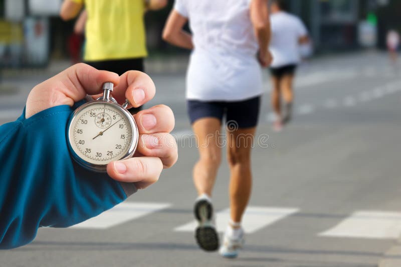 Measuring The Running Speed Of An Athlete Using A Mechanical Stopwatch.  Hand With A Stopwatch On The Background Of The Legs Of A Runner. Stock  Photo, Picture and Royalty Free Image. Image