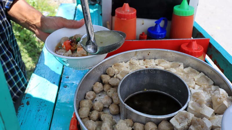 Meatball street food vendor. Asian man selling bakso by walking and pushing down the food carts