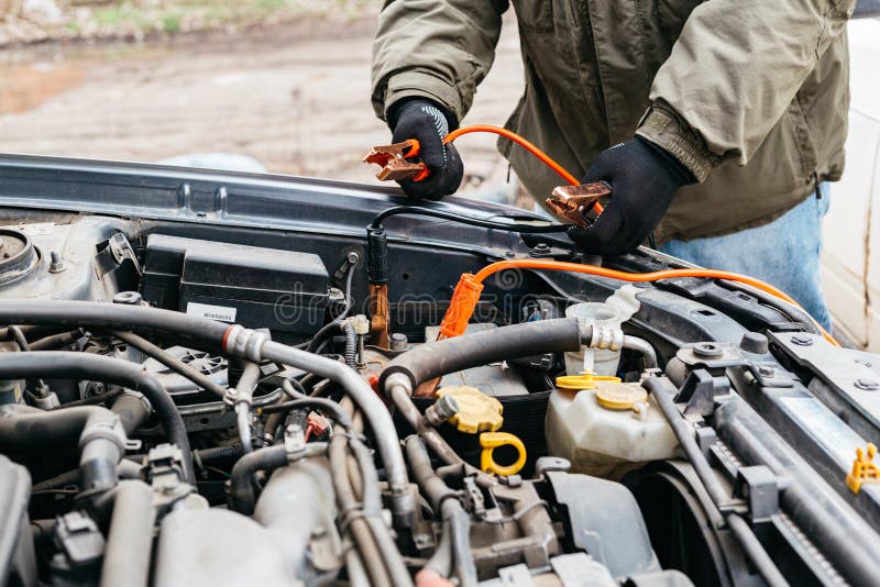 Mechanic engineer charging car battery with electricity using jumper cables outdoors. Red and black Jumper cables in male hands of