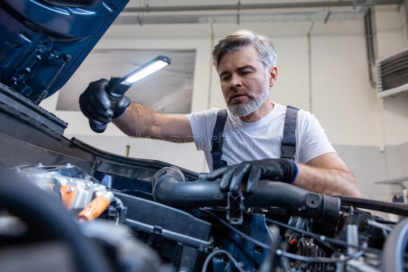 Mechanic inspecting engine with flashlight. Under open hood in auto repair shop royalty free stock photo