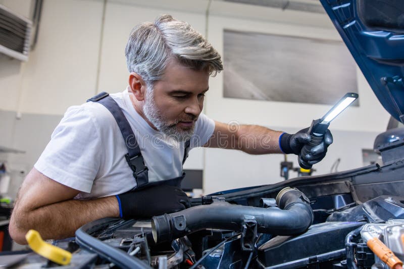 Mechanic inspecting engine with flashlight stock photos