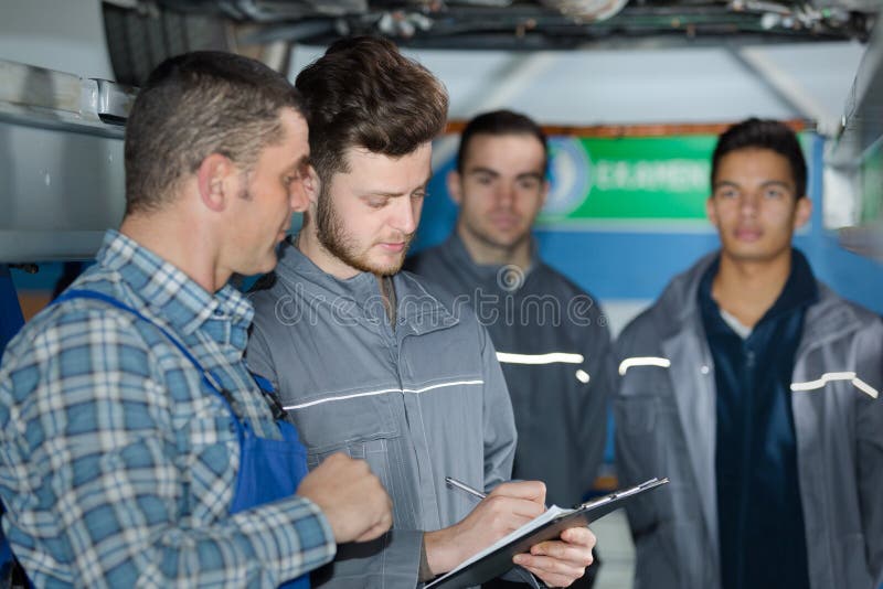 Mechanic and Male Trainee Working Underneath Car Together Stock Image