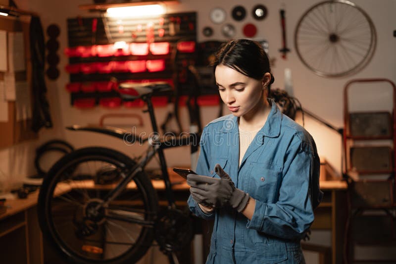 Mechanic reading a message on smartphone in bicycle workshop, she is repairing or servicing in a garage royalty free stock images