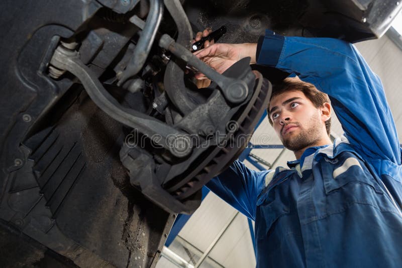 Mechanic Repairing Car In Automobile Shop. Low angle view of male mechanic repairing car in automobile shop royalty free stock photo Mechanic Repairing Car In Automobile Shop. Low angle view of male mechanic repairing car in automobile shop royalty free stock photo