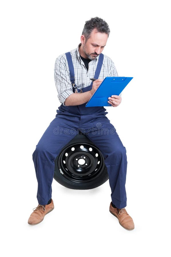 Mechanic sitting on wheel and writing on checklist stock photo Mechanic sitting on wheel and writing on checklist stock photo