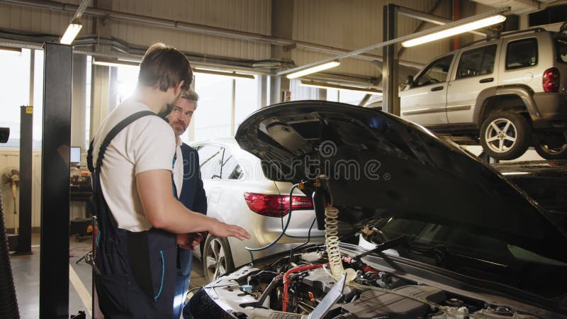 Mecánico automático muestra códigos de error de motor a un cliente masculino en un servicio de automóvil. mecánico masculino guapo