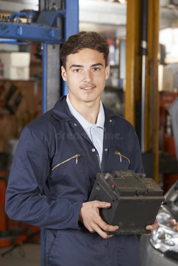 Mecánico Holding Car Battery del aprendiz en taller de reparaciones auto foto de archivo libre de regalías