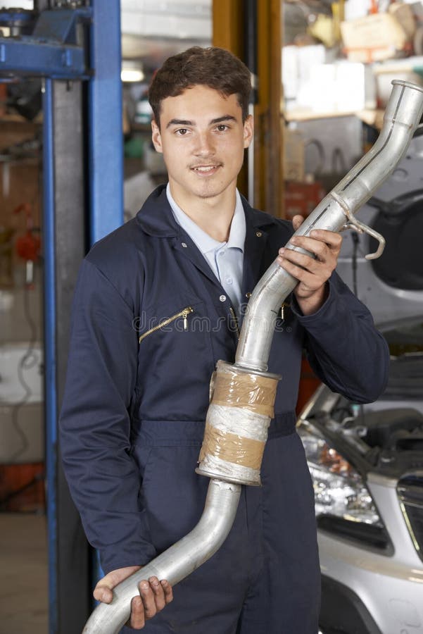 Mecánico Holding Exhaust Pipe del aprendiz en taller de reparaciones auto fotografía de archivo