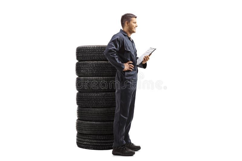 Full length profile shot of an auto mechanic in a uniform holding a clipboard and standing with a pile of tires isolated on white background. Full length profile shot of an auto mechanic in a uniform holding a clipboard and standing with a pile of tires isolated on white background