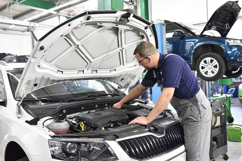 Mecânico automóvel controla o motor de um veículo - no veículo de fundo na plataforma de elevação - no local de trabalho e na pro imagens de stock royalty free Mecânico automóvel controla o motor de um veículo - no veículo de fundo na plataforma de elevação - no local de trabalho e na pro imagens de stock royalty free