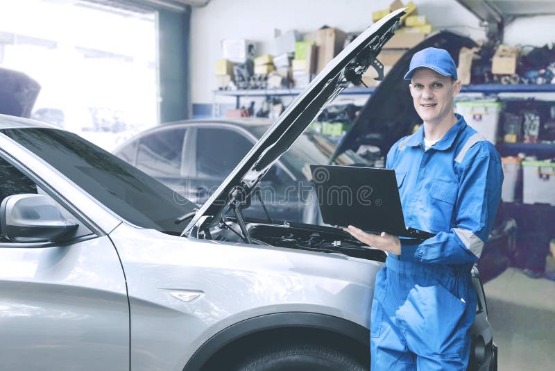 Mecânico caucasiano que verifica o motor de automóveis usando o portátil do computador na oficina de reparações fotos de stock Mecânico caucasiano que verifica o motor de automóveis usando o portátil do computador na oficina de reparações fotos de stock
