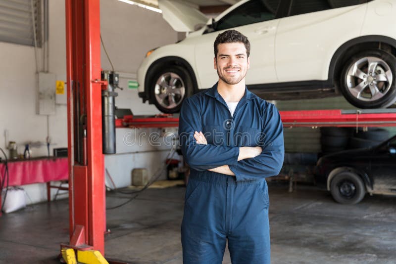 Smiling mechanic in uniform standing with hands folded in auto shop. Smiling mechanic in uniform standing with hands folded in auto shop