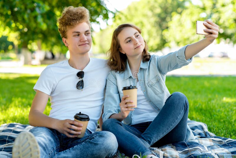 Med en flicka i sommar i natur De sitter på en filt Han rymmer koppar med kaffe eller te i hans händer Han tar bilder royaltyfri bild Med en flicka i sommar i natur De sitter på en filt Han rymmer koppar med kaffe eller te i hans händer Han tar bilder royaltyfri bild