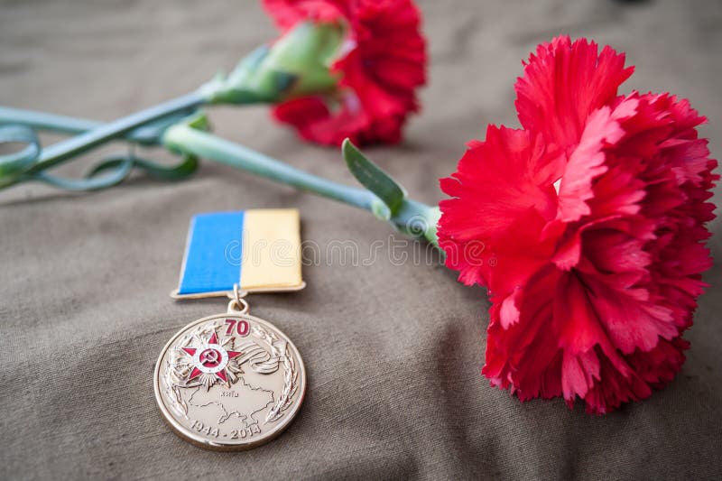 Medaglia 70 anni di liberazione dell'Ucraina dai Nazi e da due garofani rossi fotografia stock Medaglia 70 anni di liberazione dell'Ucraina dai Nazi e da due garofani rossi fotografia stock