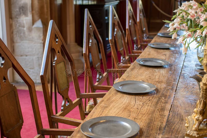 Medieval dining table and chairs. Mediaeval period banquet table set with metal plates. Fine historic fraternal banqueting hall. Secret society chamber with anonymous empty seats. Medieval dining table and chairs. Mediaeval period banquet table set with metal plates. Fine historic fraternal banqueting hall. Secret society chamber with anonymous empty seats.