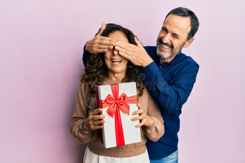 Media edad hispano pareja sorprendente con guiño de regalo mirando a la cámara con expresión sexy alegre y feliz cara imágenes de archivo libres de regalías