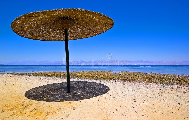 Canopy parasol umbrella shade on sandy beach against a blue sky. Shadow detail direct below canopy indication mid day sun. Canopy parasol umbrella shade on sandy beach against a blue sky. Shadow detail direct below canopy indication mid day sun.