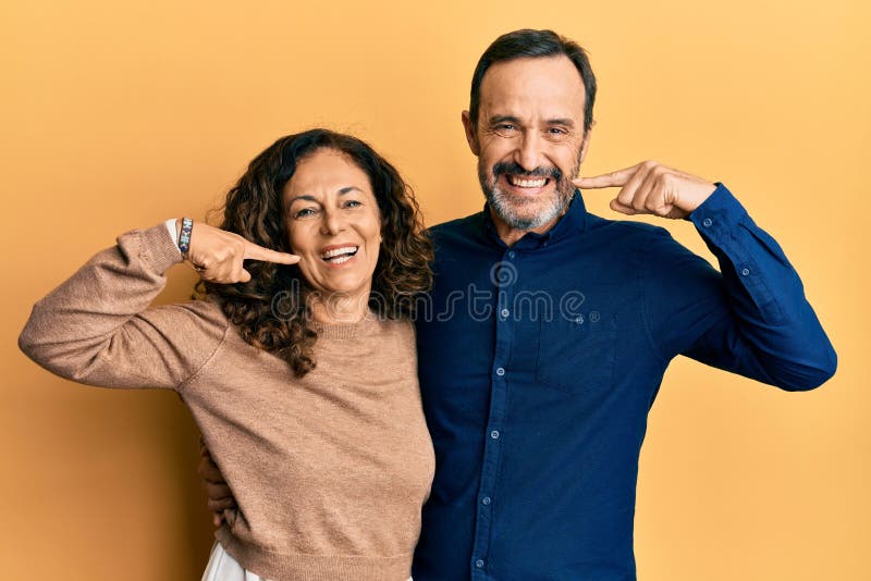 Mediana edad hispano pareja con ropa casual sonriendo alegre mostrando y señalando con los dedos los dientes y la boca imagen de archivo