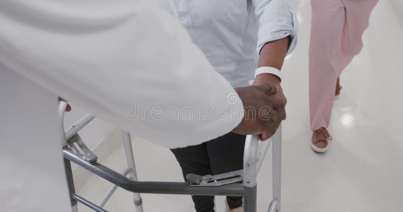 Mediana sección de doctores masculinos diversos que ayudan a las pacientes de edad avanzada a usar el cuadro de caminar cámara len almacen de video