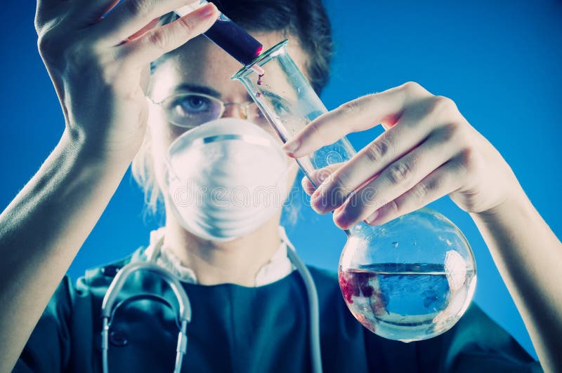 Medic in laboratory. Medic in green gown working in laboratory with red liquid. Blue background. Landscape orientation Medic in laboratory. Medic in green gown working in laboratory with red liquid. Blue background. Landscape orientation
