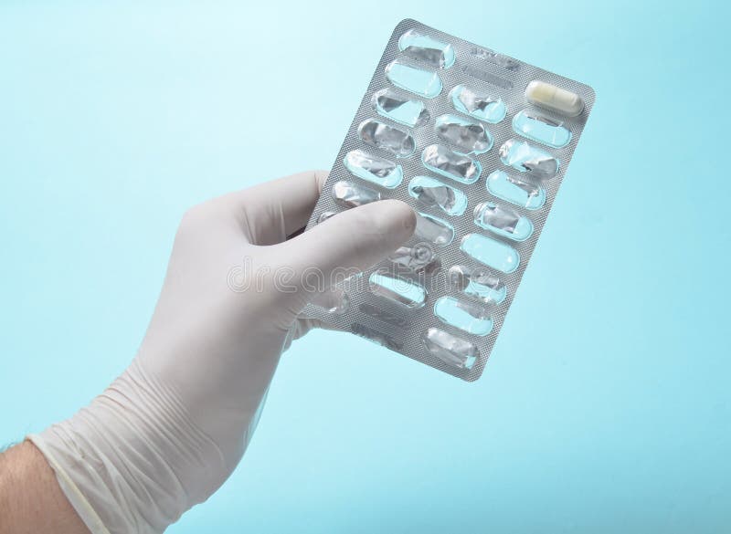 A medic& x27;s hand with white latex gloves holds an empty blister of pills on a blue background royalty free stock images A medic& x27;s hand with white latex gloves holds an empty blister of pills on a blue background royalty free stock images