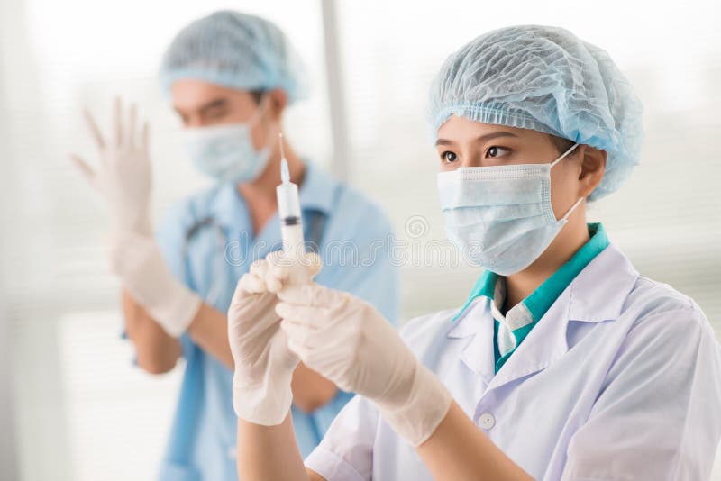 Nurse filling the syringe while male doctor getting ready for a medical procedure. Nurse filling the syringe while male doctor getting ready for a medical procedure