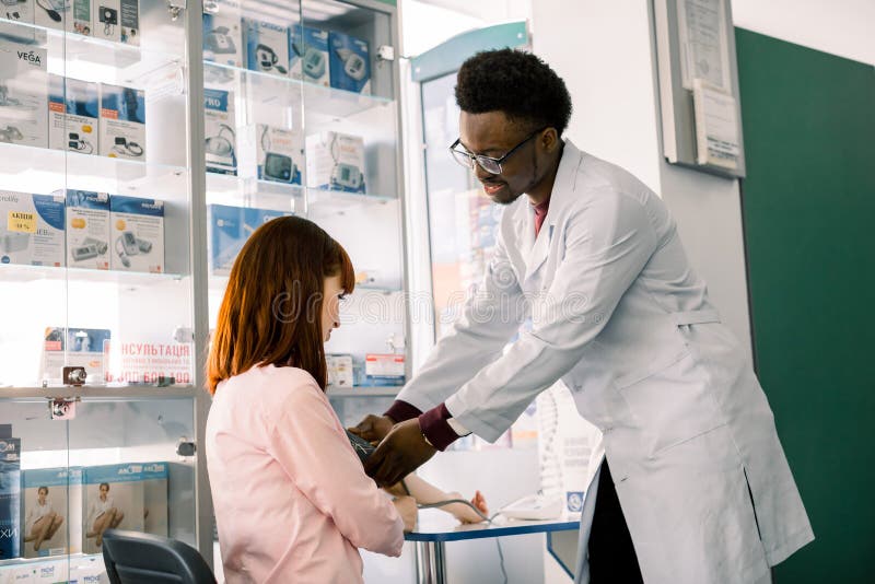 Medici?n de la presi?n arterial Paciente africano del farmacéutico o del doctor y de la mujer joven del hombre Fondo moderno de l fotografía de archivo Medici?n de la presi?n arterial Paciente africano del farmacéutico o del doctor y de la mujer joven del hombre Fondo moderno de l fotografía de archivo