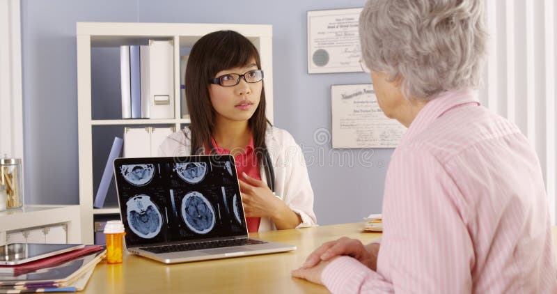 Medico asiatico che spiega le scansioni del cervello al paziente anziano fotografie stock libere da diritti Medico asiatico che spiega le scansioni del cervello al paziente anziano fotografie stock libere da diritti