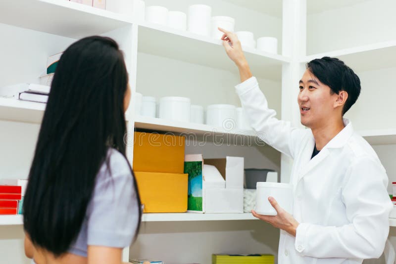 Medico asiatico del farmacista in abito professionale che spiega e che esprime parere con il cliente femminile nel negozio della immagini stock Medico asiatico del farmacista in abito professionale che spiega e che esprime parere con il cliente femminile nel negozio della immagini stock
