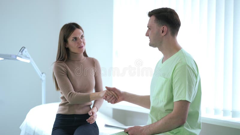 Medico caucasico sorridente che stringe la mano al paziente in ospedale salutando una donna che se ne va al rallentatore. positivo