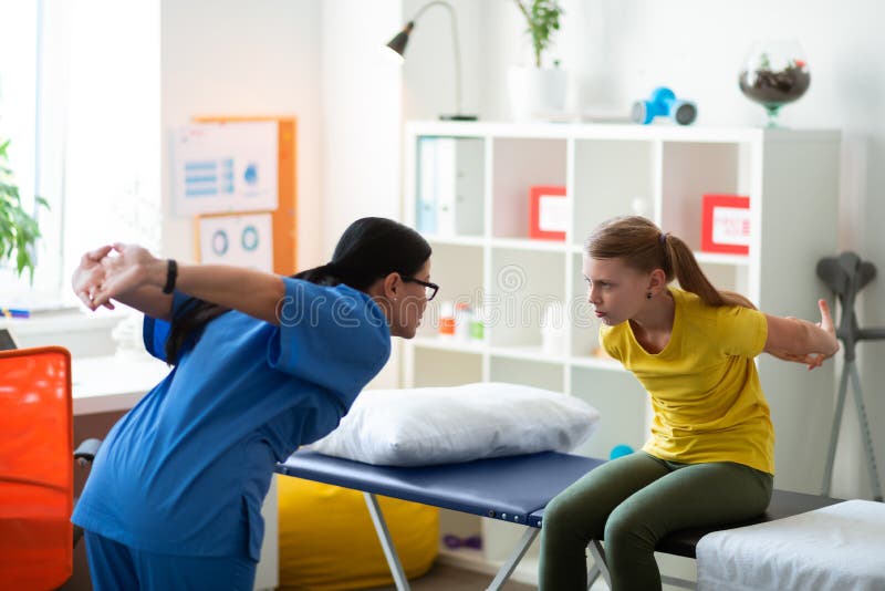Medico dai capelli lunghi preoccupantesi attento che corregge posizione della bambina fotografie stock libere da diritti Medico dai capelli lunghi preoccupantesi attento che corregge posizione della bambina fotografie stock libere da diritti