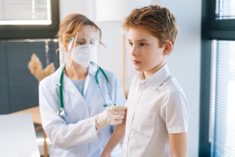 Medico donna con uniforme bianca e maschera di sicurezza che applica gesso sulla spalla di un bambino dopo la vaccinazione fotografia stock