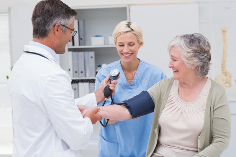 Medico ed infermiere che controllano pressione sanguigna senior dei pazienti fotografia stock libera da diritti Medico ed infermiere che controllano pressione sanguigna senior dei pazienti fotografia stock libera da diritti